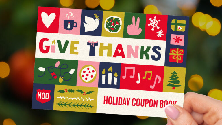 Hand holding our coupon book that says Give Thanks.